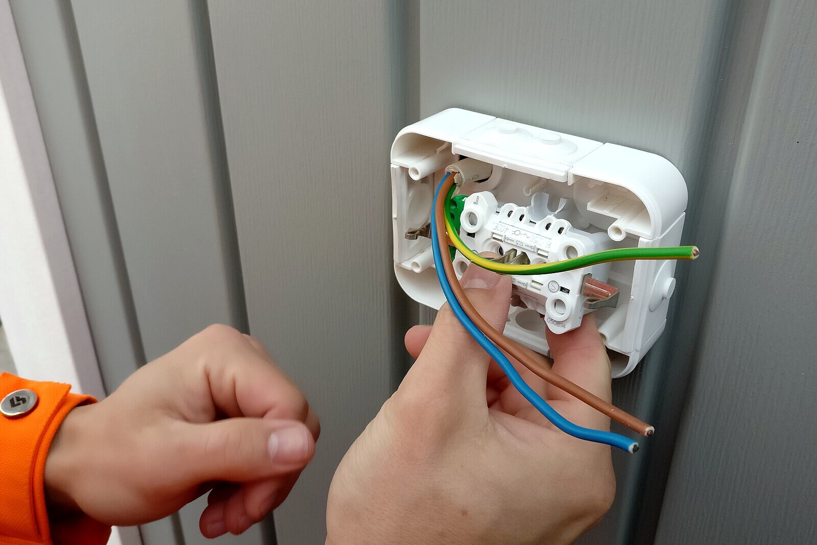 Електротехник в оранжева работна униформа свързва жици на ел. контакт